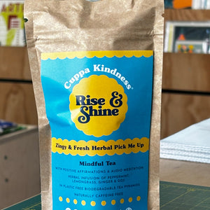 Cuppa Kindness Tea package with teal and yellow 'Rise & Shine' branding on a blurred background