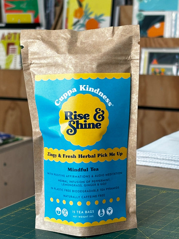 Cuppa Kindness Tea package with teal and yellow 'Rise & Shine' branding on a blurred background